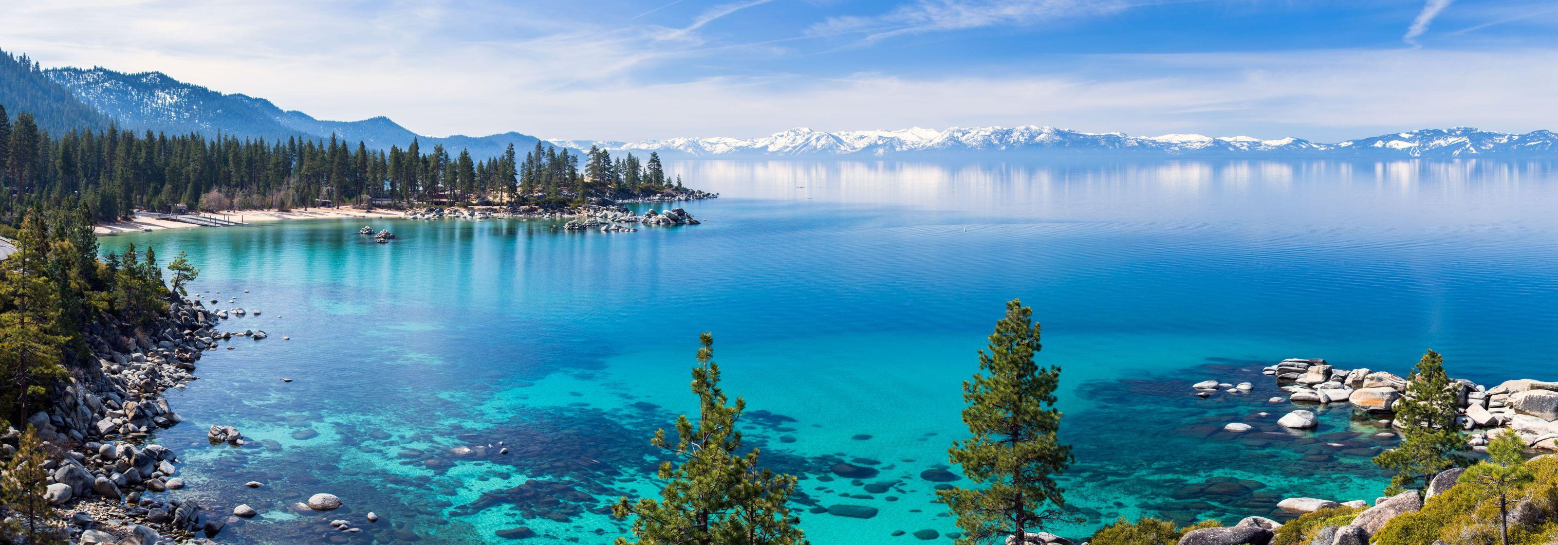 Panoramic view of Lake Tahoe\'s other side featuring mountains, trails, and ski resorts